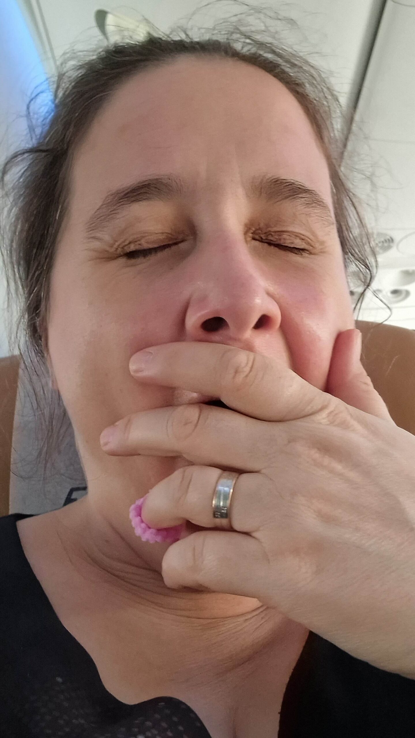 Selfie von einer gähnenden Frau, sie hält die Hand vor den Mund und hat die Augen geschlossen
